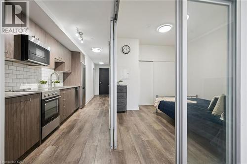 Kitchen and living area featuring wood-finish flooring, stainless steel appliances, subway tile backsplash, and wood-finish cabinetry - 15 Wellington Street S Unit# 903, Kitchener, ON - Indoor Photo Showing Kitchen With Stainless Steel Kitchen With Upgraded Kitchen