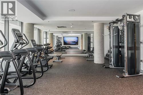 Fitness center featuring resilient rubber flooring, full-height windows, a large wall-mounted screen, and a selection of cardio and strength training equipment - 15 Wellington Street S Unit# 903, Kitchener, ON - Indoor Photo Showing Gym Room