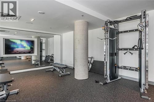 Fitness area featuring rubberized flooring, mirrored wall, and a large wall-mounted screen - 15 Wellington Street S Unit# 903, Kitchener, ON - Indoor Photo Showing Gym Room