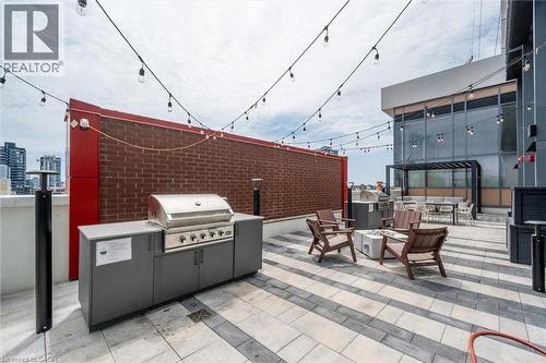 Rooftop patio featuring an outdoor kitchen with an integrated stainless steel grill, a fire pit, string lighting, and patterned paver flooring - 15 Wellington Street S Unit# 903, Kitchener, ON - Outdoor With Exterior