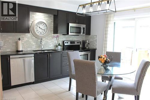 Dark wood-finish cabinetry with stainless steel hardware, mosaic tile backsplash, stainless steel appliances, and tile flooring - 12 Poplar Drive Unit# 21, Cambridge, ON - Indoor