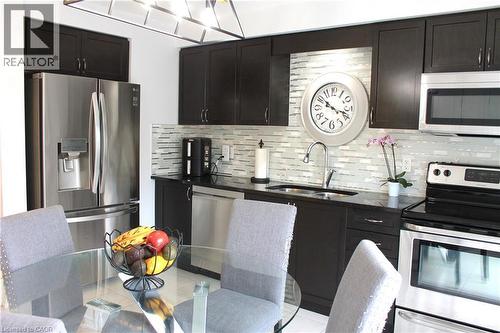 Modern kitchen featuring sleek dark cabinetry, stainless steel appliances including a French-door refrigerator and convection range, linear tile backsplash, and quartz countertops - 12 Poplar Drive Unit# 21, Cambridge, ON - Indoor Photo Showing Kitchen With Stainless Steel Kitchen With Upgraded Kitchen