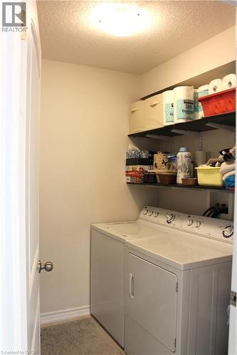 Dedicated laundry room featuring stacked washer and dryer appliances, white cabinetry with ample storage, floating black shelving with organized storage capacity, quartz countertop work surface, and r - 12 Poplar Drive Unit# 21, Cambridge, ON - Indoor Photo Showing Laundry Room