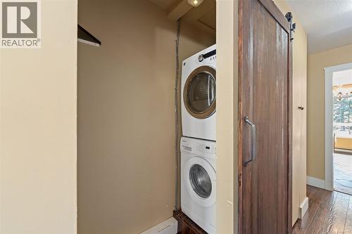 Stackable washer and dryer unit, wood-finish flooring, recessed lighting, and a barn door with a dark-finish handle - 4105 Ross Rd, Nanaimo, BC - Indoor Photo Showing Laundry Room