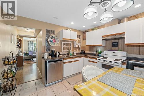 Kitchen with white cabinetry, stainless steel dishwasher, white range, tile flooring, and a multi-light ceiling fixture - 4105 Ross Rd, Nanaimo, BC - Indoor Photo Showing Kitchen With Double Sink