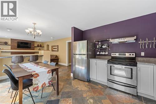 Stainless steel appliances, built-in shelving, stone tile flooring, and a breakfast bar with built-in seating - 4105 Ross Rd, Nanaimo, BC - Indoor Photo Showing Kitchen