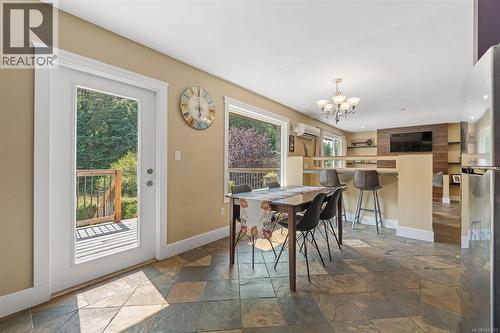 French door leading to a wooden deck, Large window with views of Trillium park, natural stone floor tiles, recessed wall shelving, and a multi-light chandelier - 4105 Ross Rd, Nanaimo, BC - Indoor Photo Showing Dining Room