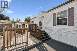 Wood deck and ramp with railings, exterior storage shed, white vinyl siding, brown louvered shutters, and dark steps - 
