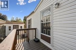 Deck with wood-finish railing, white vinyl siding, outdoor wall light fixture, storm door with arched transom, and a detached shed - 