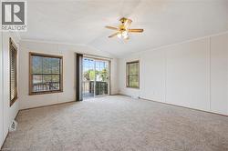 Spacious room featuring neutral carpeting, a ceiling fan with integrated lighting, and multiple windows with wood trim - 