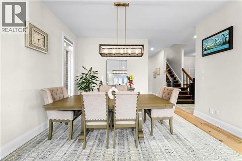 Formal dining area featuring a linear chandelier, light wood-finish flooring, and a stairway with dark wood treads and a wood railing - 130 Pondcliffe Drive, Kitchener, ON - Indoor Photo Showing Dining Room