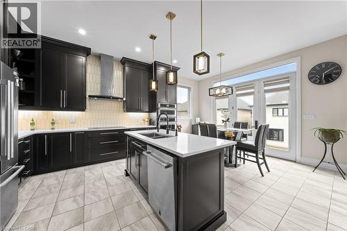 Modern kitchen featuring dark cabinetry, stainless steel appliances, a center island with sink, stylish pendant lighting, and light-toned tile flooring - 130 Pondcliffe Drive, Kitchener, ON - Indoor Photo Showing Kitchen With Double Sink With Upgraded Kitchen
