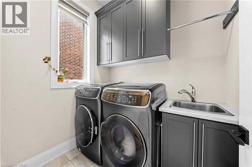 Laundry area featuring dark gray cabinetry, a utility sink with a chrome faucet, a wall-mounted drying rack, and a window with white trim - 130 Pondcliffe Drive, Kitchener, ON - Indoor Photo Showing Laundry Room