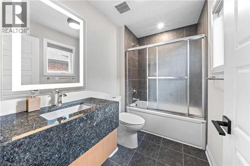 Bathroom featuring a lighted vanity mirror, under-mount sink, dark stone countertop, and a tiled tub/shower combination with sliding glass doors - 130 Pondcliffe Drive, Kitchener, ON - Indoor Photo Showing Bathroom