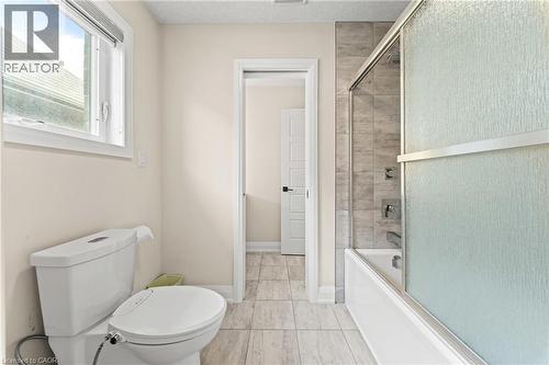 Full bathroom featuring a white ceramic toilet, a window with a white frame, light-toned wall paint, a shower-over-tub combination with a sliding glass door, and a light gray tiled floor - 130 Pondcliffe Drive, Kitchener, ON - Indoor Photo Showing Bathroom