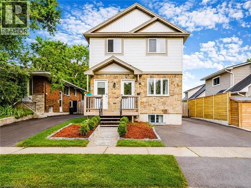 Two-story facade with stone and siding finishes, featuring a porch with railings, landscaped front beds, and a paved driveway - 67 Kinzie Avenue, Kitchener, ON - Outdoor With Facade