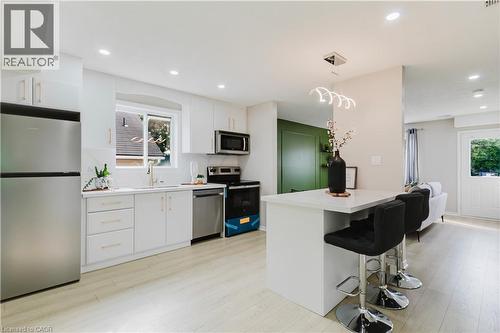 Bright kitchen featuring white cabinetry, stainless steel appliances, a white island with seating, and wood-finish flooring - 67 Kinzie Avenue, Kitchener, ON - Indoor Photo Showing Kitchen