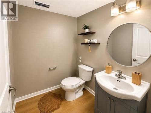 Wood-finish flooring, wall-mounted floating shelves, integrated sink, vanity with cabinet storage, and an oval mirror - 67 Kinzie Avenue, Kitchener, ON - Indoor Photo Showing Bathroom
