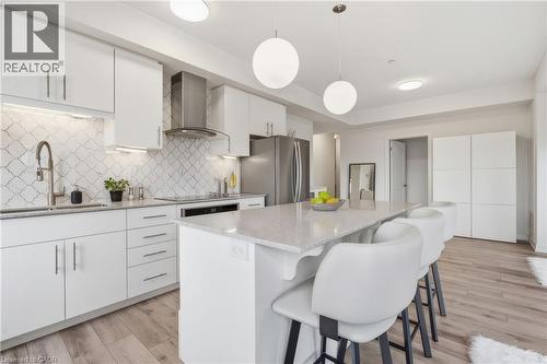 Modern kitchen featuring white cabinetry, stainless steel appliances, a tile backsplash, wood-finish flooring, and a large center island - 251 Northfield Drive E Unit# 312, Waterloo, ON 