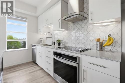 Modern kitchen featuring white cabinetry, light-colored countertops, a tile backsplash, stainless steel appliances, and wood-finish flooring - 251 Northfield Drive E Unit# 312, Waterloo, ON 