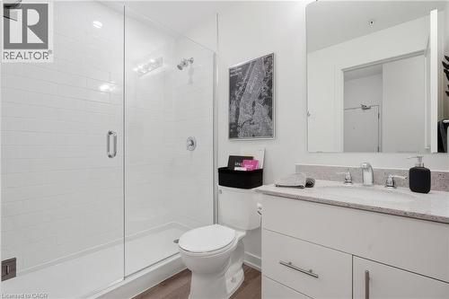 Glass-enclosed shower with white subway tile, single vanity with light-colored countertop, integrated sink, and wood-finish flooring - 251 Northfield Drive E Unit# 312, Waterloo, ON 