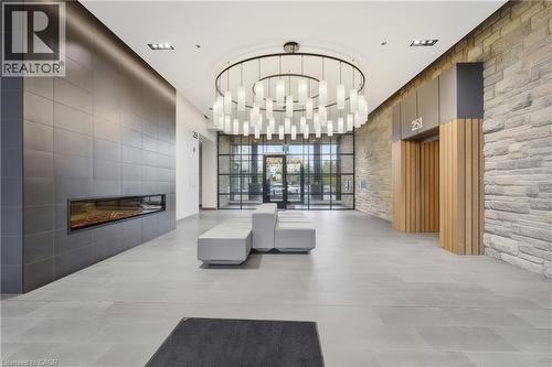 Spacious lobby featuring a linear electric fireplace, large format tile flooring, stone accent wall, and a round chandelier with multiple lights - 251 Northfield Drive E Unit# 312, Waterloo, ON 