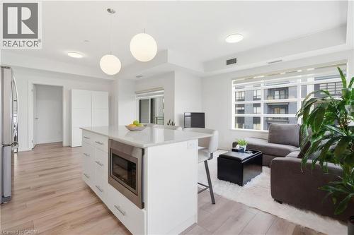 Open-concept living area with wood-finish flooring, a kitchen island with stone countertop, stainless steel microwave drawer, and large windows - 251 Northfield Drive E Unit# 312, Waterloo, ON 
