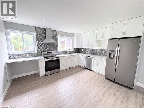 Updated kitchen featuring white shaker cabinetry, stainless steel appliances, herringbone tile backsplash, and wood-finish flooring - 216 Brunswick Crescent, London, ON - Indoor Photo Showing Kitchen