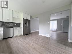 Modern kitchen with white cabinetry, stainless steel appliances, herringbone tile backsplash, and wood-finish flooring - 