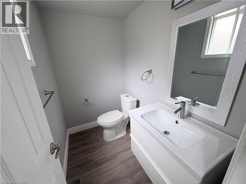 Vanity with integrated sink and chrome faucet, rectangular mirror with decorative frame, wood-finish flooring, and a white toilet - 216 Brunswick Crescent, London, ON - Indoor Photo Showing Bathroom