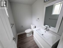 Vanity with integrated sink and chrome faucet, rectangular mirror with decorative frame, wood-finish flooring, and a white toilet - 