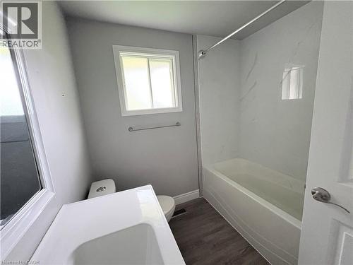 Modern bathroom featuring a white vanity with integrated sink, white bathtub with a marble-patterned surround, wood-finish flooring, and a white framed window - 216 Brunswick Crescent, London, ON - Indoor Photo Showing Bathroom