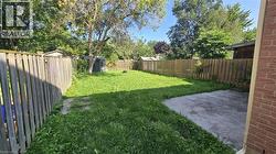 Expansive backyard featuring a lush lawn, privacy fencing, mature trees, and a concrete patio - 