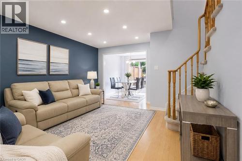 Recessed lighting, wood-finish flooring, staircase with wood railing, blue accent wall, and a dining area with a glass-top table - 1793 Creek Way, Burlington, ON - Indoor Photo Showing Living Room