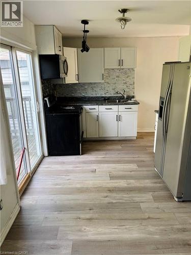 Kitchen featuring wood-finish flooring, white cabinetry, dark countertops, a tiled backsplash, and stainless steel appliances - 218 East 8Th Street, Hamilton, ON - Indoor Photo Showing Kitchen