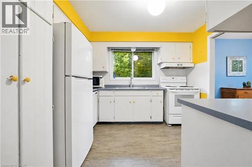 Kitchen featuring wood-finish flooring, white cabinetry with yellow knobs, a white refrigerator, and a white oven with an overhead range hood - 11 Kimbermount Drive, St. Catharines, ON - Indoor Photo Showing Kitchen With Double Sink