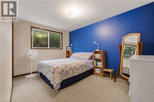 Carpeted bedroom featuring a large window with brown trim, a vibrant blue accent wall, and a flush-mount ceiling light fixture - 11 Kimbermount Drive, St. Catharines, ON - Indoor Photo Showing Bedroom