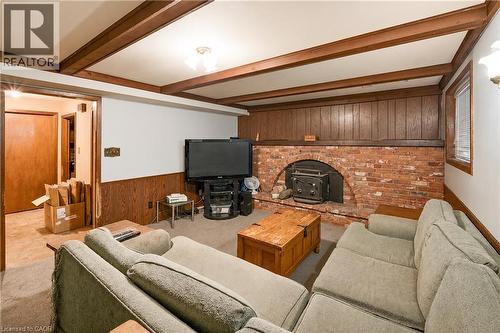 Living area featuring a brick fireplace with a wood-burning stove insert, wood paneling, and wood-beam ceiling details - 11 Kimbermount Drive, St. Catharines, ON - Indoor Photo Showing Living Room With Fireplace