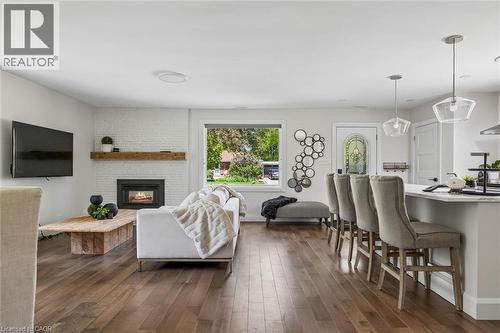 Wood-finish flooring throughout, a white brick fireplace with a wood-beam mantel, a kitchen island with seating, and clear glass pendant lighting - 90 Dean Avenue, Guelph, ON - Indoor With Fireplace
