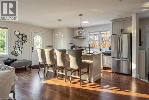 Hardwood-finish flooring extending into the kitchen, kitchen island with counter seating, stainless steel appliances, pendant lighting, and gray cabinetry - 90 Dean Avenue, Guelph, ON - Indoor