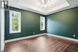 Tray ceiling with a contemporary chandelier, rich green walls, and wood-finish flooring - 
