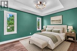 Tray ceiling with a decorative light fixture, wood-finish flooring, and white trim - 