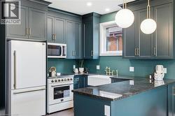 Kitchen featuring dark cabinetry, white appliances, a farmhouse sink, stone countertops, and spherical pendant lighting - 
