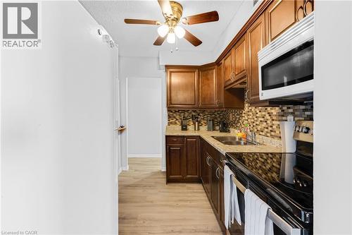 Galley kitchen featuring wood-finish cabinetry, granite-style countertops, mosaic tile backsplash, and wood-finish flooring - 975 Warwick Court Unit# 708, Burlington, ON - Indoor Photo Showing Kitchen With Double Sink