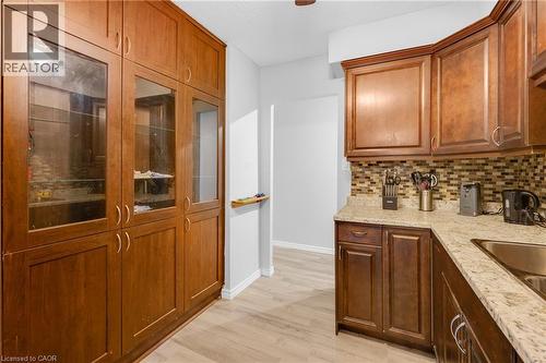 Wood-finish flooring, full-height cabinetry with glass-front uppers, granite-style countertops, and a mosaic tile backsplash - 975 Warwick Court Unit# 708, Burlington, ON - Indoor Photo Showing Kitchen