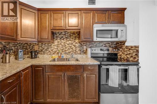 Full-height wood cabinetry with crown molding, mosaic tile backsplash, double basin stainless steel sink, built-in microwave, and stainless steel electric range - 975 Warwick Court Unit# 708, Burlington, ON - Indoor Photo Showing Kitchen