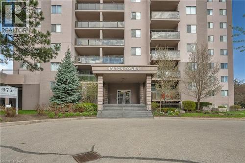 Building exterior featuring a covered entrance with columns, glass balcony railings, and mature landscaping - 975 Warwick Court Unit# 708, Burlington, ON - Outdoor With Balcony With Facade