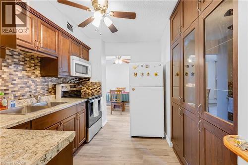 Kitchen featuring wood-finish cabinetry, light-toned wood-finish flooring, and speckled countertops - 975 Warwick Court Unit# 708, Burlington, ON - Indoor Photo Showing Kitchen