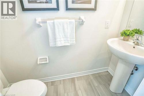 Pedestal sink with chrome faucet, toilet, wall-mounted towel bar, and wood-finish flooring - 525 Red Elm Road, Shelburne, ON - Indoor Photo Showing Bathroom