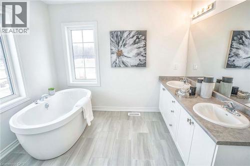 Freestanding soaking tub, dual windows, wood-finish flooring, double vanity with integrated sinks, and polished chrome fixtures - 525 Red Elm Road, Shelburne, ON - Indoor Photo Showing Bathroom